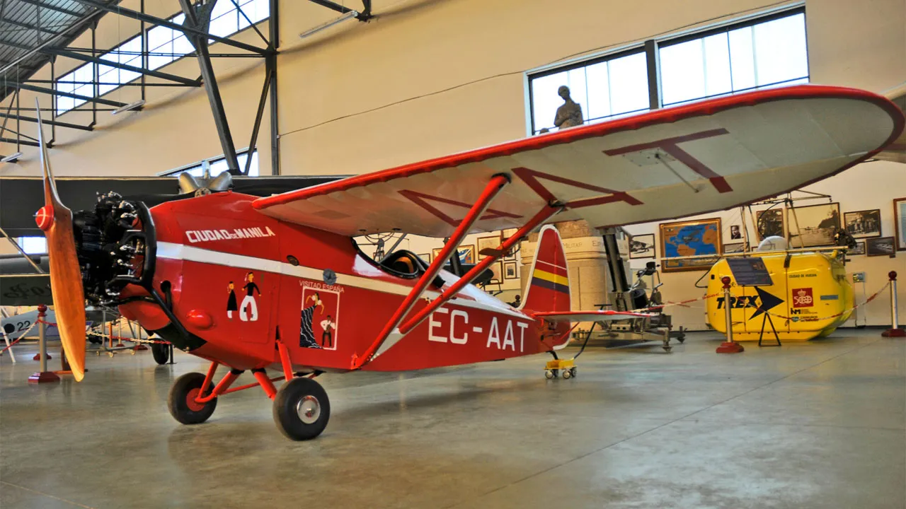 Een rood-wit vintage vliegtuig met registratie EC-AAT tentoongesteld in een museumhangaar