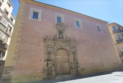 Fachada de ladrillo rosado de un edificio histórico que presenta un gran portal de piedra ornamentado y ventanas rectangulares bajo un cielo azul despejado.