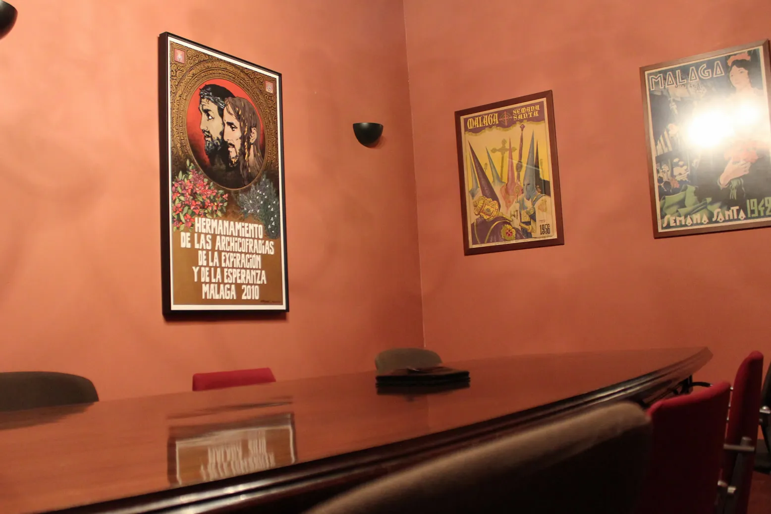Sala de reuniones interior con una larga mesa de conferencias de madera y carteles de Semana Santa enmarcados sobre paredes de color terracota