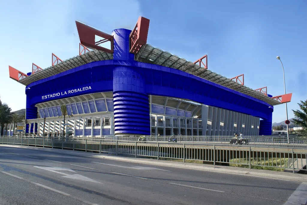 Vista exterior del estadio azul Estadio La Rosaleda con soportes estructurales rojos y una calle en primer plano.