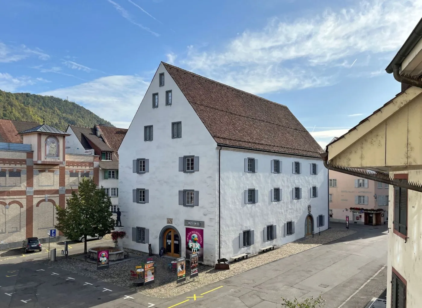 Wit gebouw met meerdere verdiepingen, een steil bruin pannendak en grijze luiken: het Museum.BL in Liestal, met een banner bij de boogvormige ingang en een geplaveide binnenplaats.