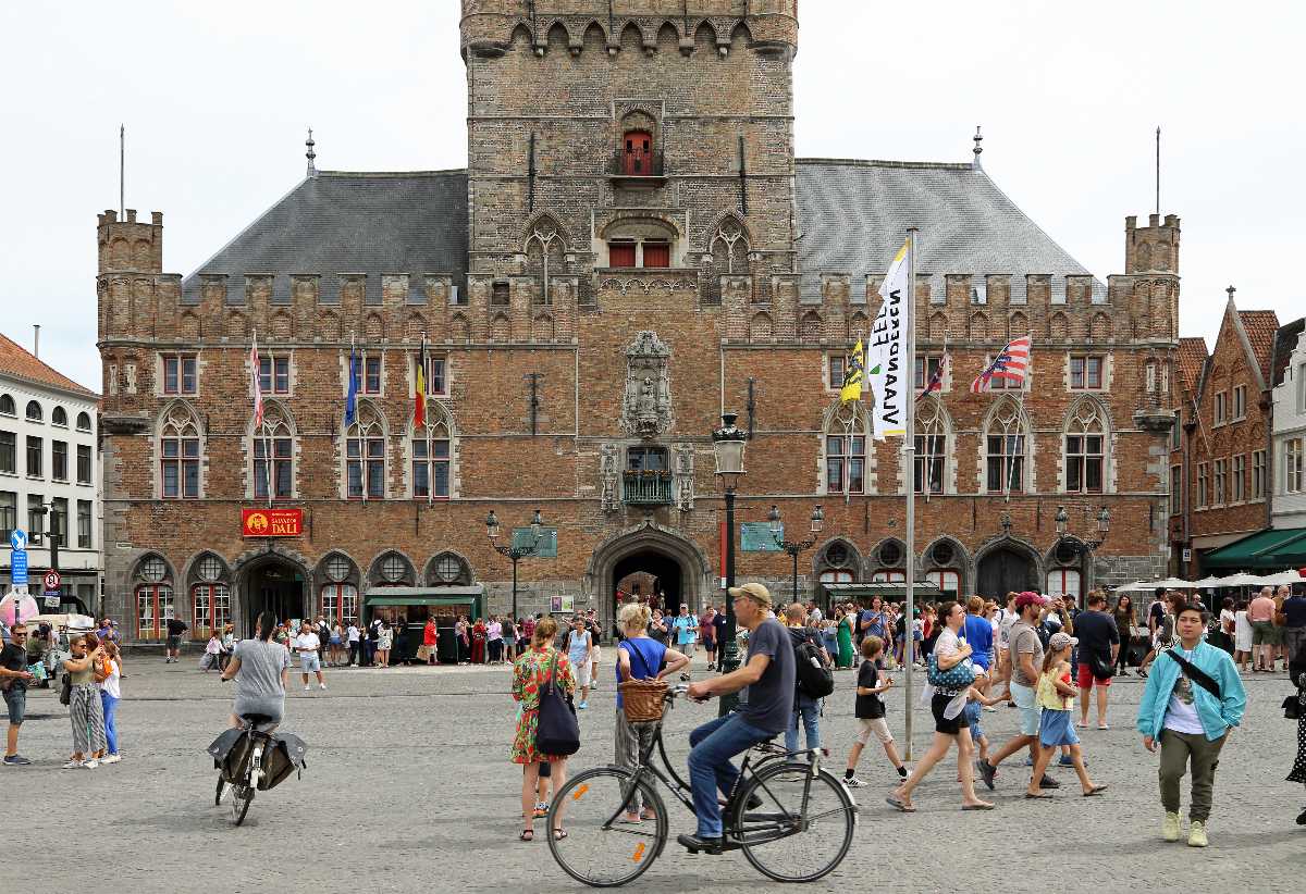 Vista exterior del histórico edificio de ladrillo Provinciaal Hof en la plaza Markt en Brujas, con personas caminando y andando en bicicleta en primer plano