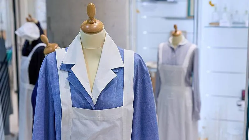 Mannequins dressed in historical nursing uniforms, including a blue tunic with a white apron and collar, in a museum display.