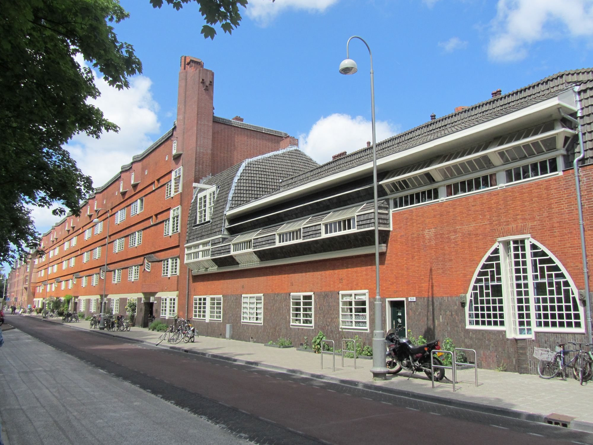 Red brick building with arched windows and a chimney, part of Museum Het Schip on a street corner.