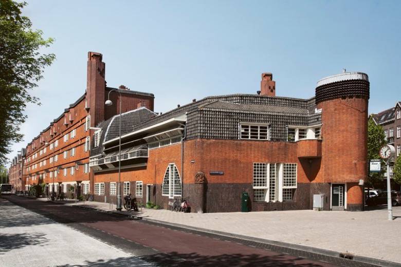 Red brick building with ornate architectural details and a rounded tower, characteristic of the Amsterdam School style.