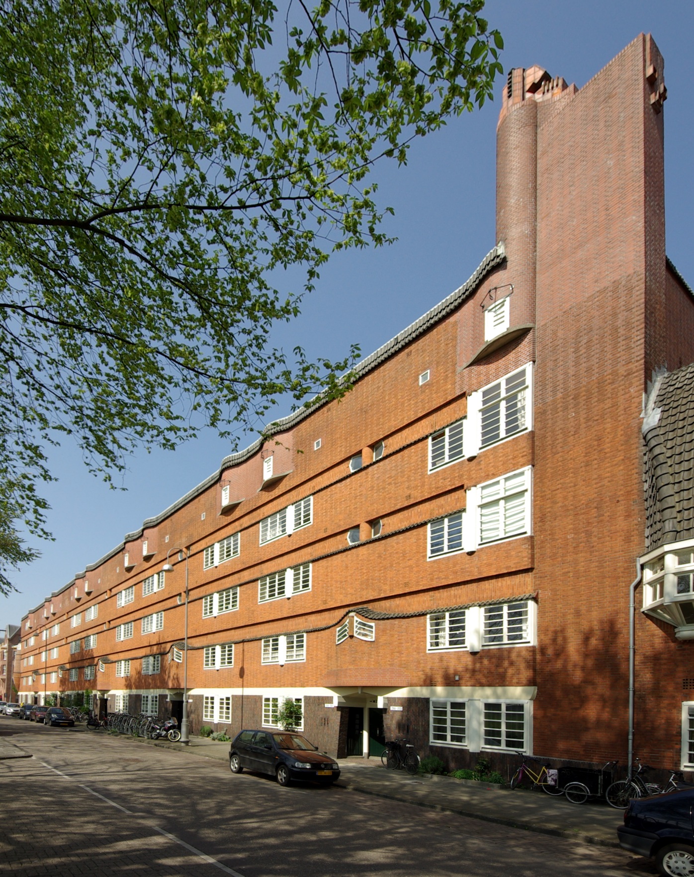 Red brick Amsterdam School style building with white-framed windows, distinctive tower, and curved facade under blue sky. Museum Het Schip exterior.