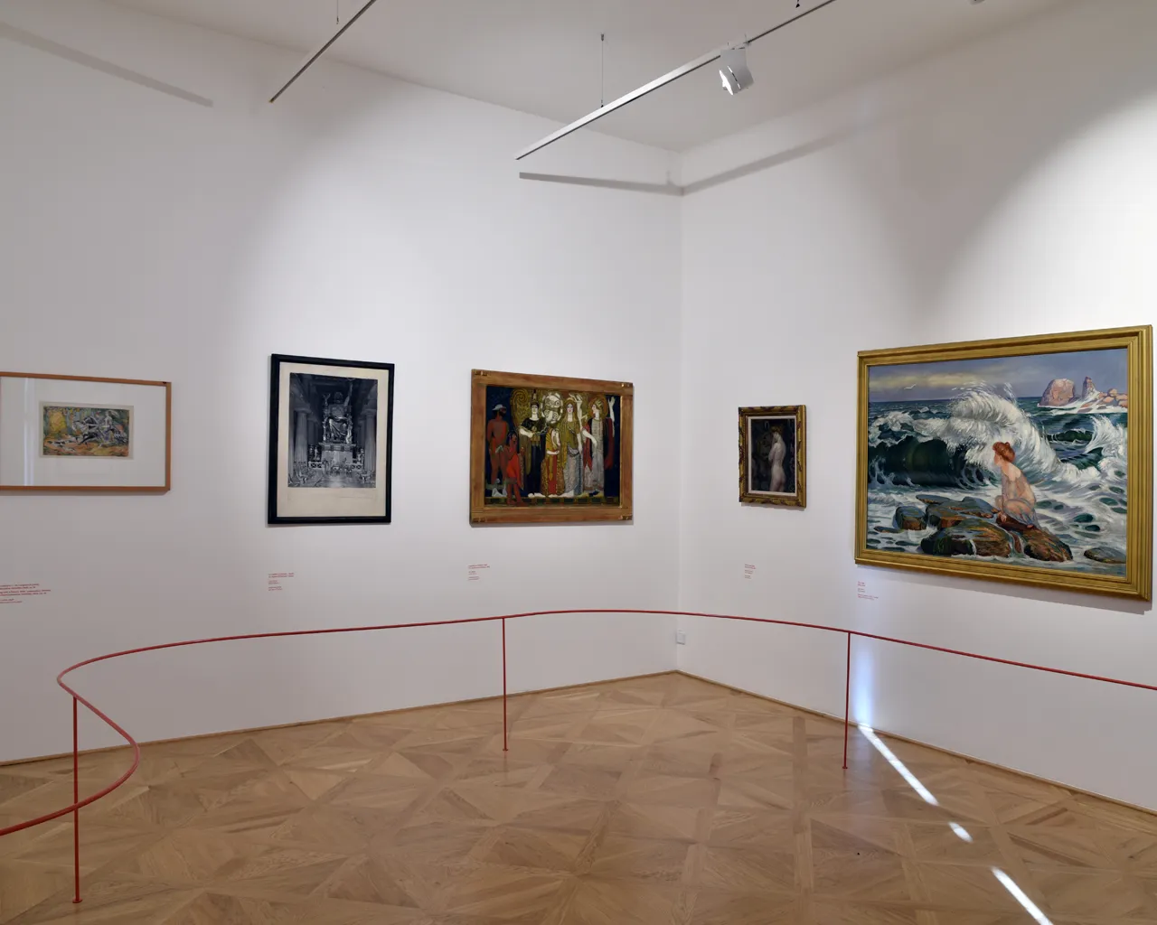 Galería de arte con varias pinturas en paredes blancas, una barrera de cuerda roja y un suelo de madera