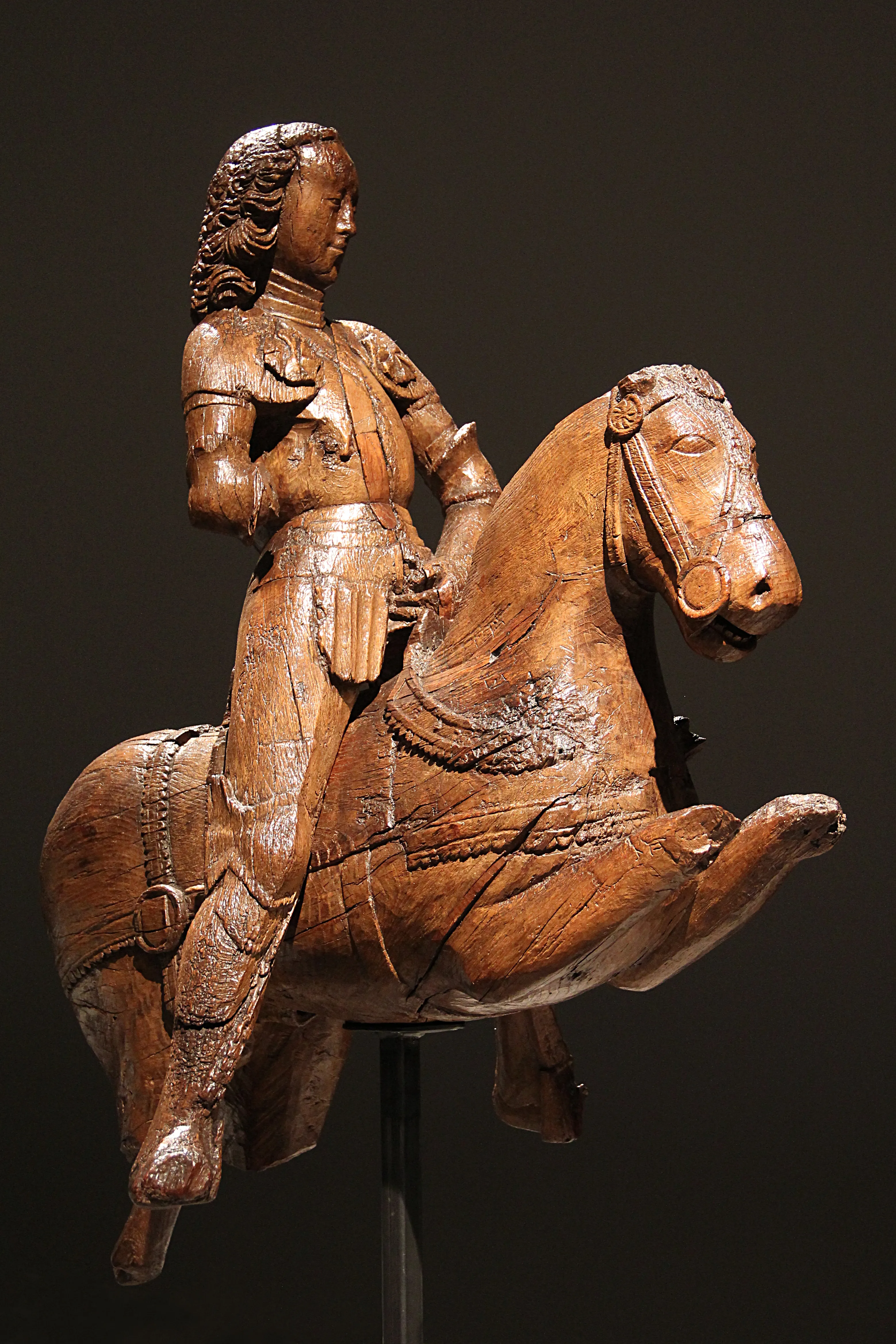 Escultura de madera de un caballero armado a caballo que representa a San Jorge, exhibida sobre un fondo oscuro