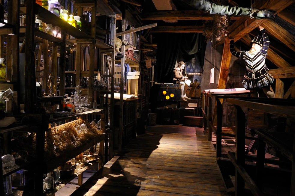 narrow wooden corridor inside a museum with shelves of alchemical instruments and a mannequin in historical clothing