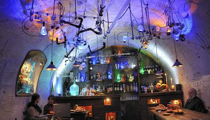 dimly lit interior with arched stone walls, hanging glass bottles and light bulbs, and visitors seated at tables