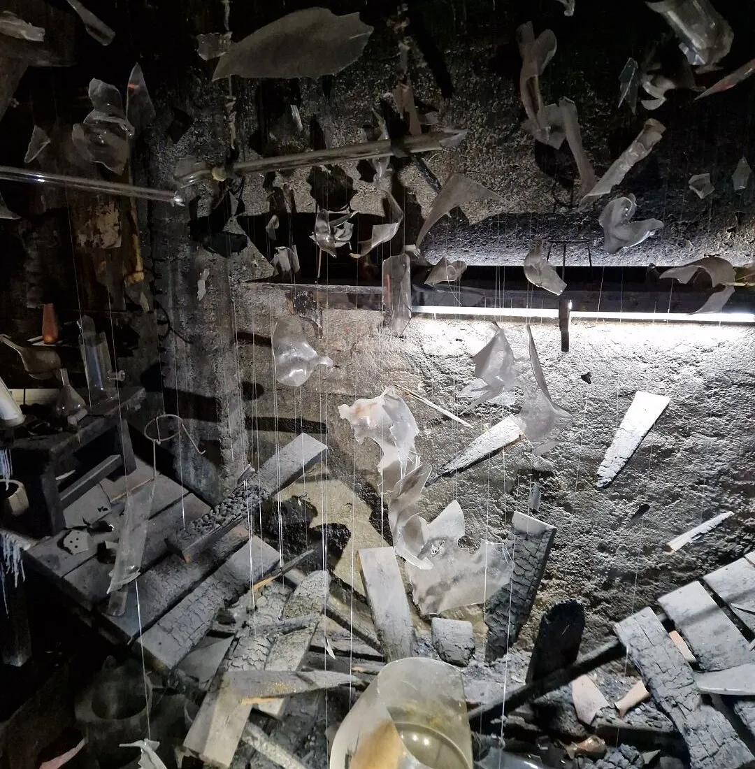 shattered glass and debris in a dark indoor space with hanging fragments and a bright light strip