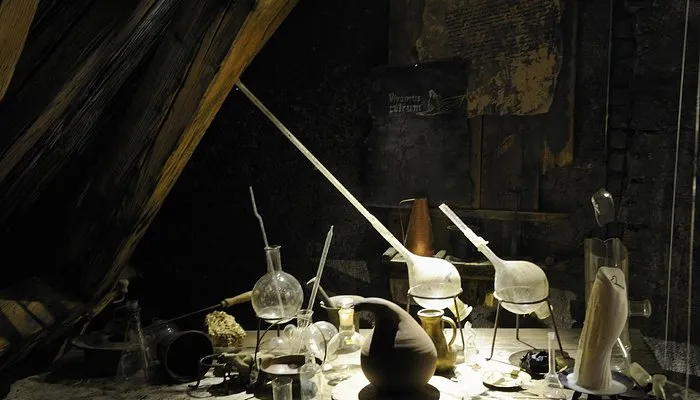 alchemical equipment including glass flasks, a long tube, and a clay vessel on a table in a dark room