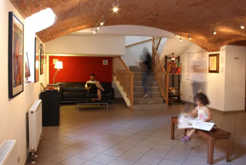 Interior lobby with arched wooden ceiling, red wall, framed art, and people in a museum