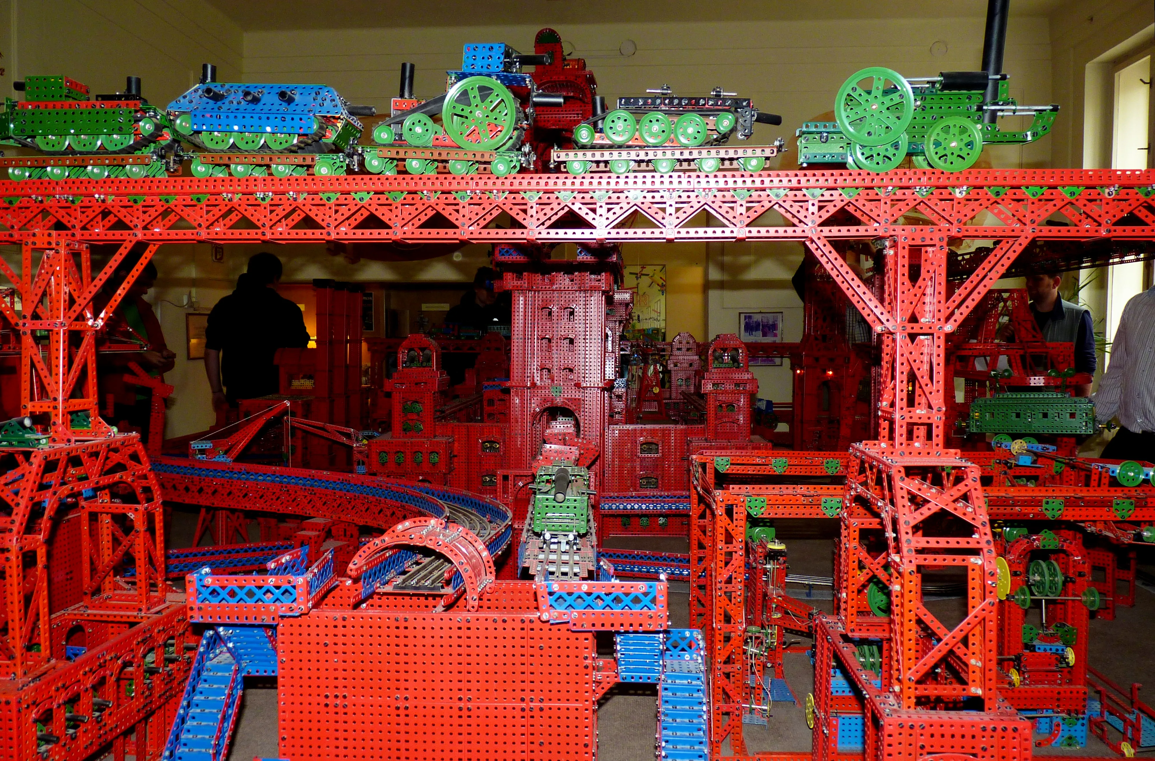 Een grote LEGO-treintentoonstelling met groene en blauwe treinen op een rode brugconstructie in een museum