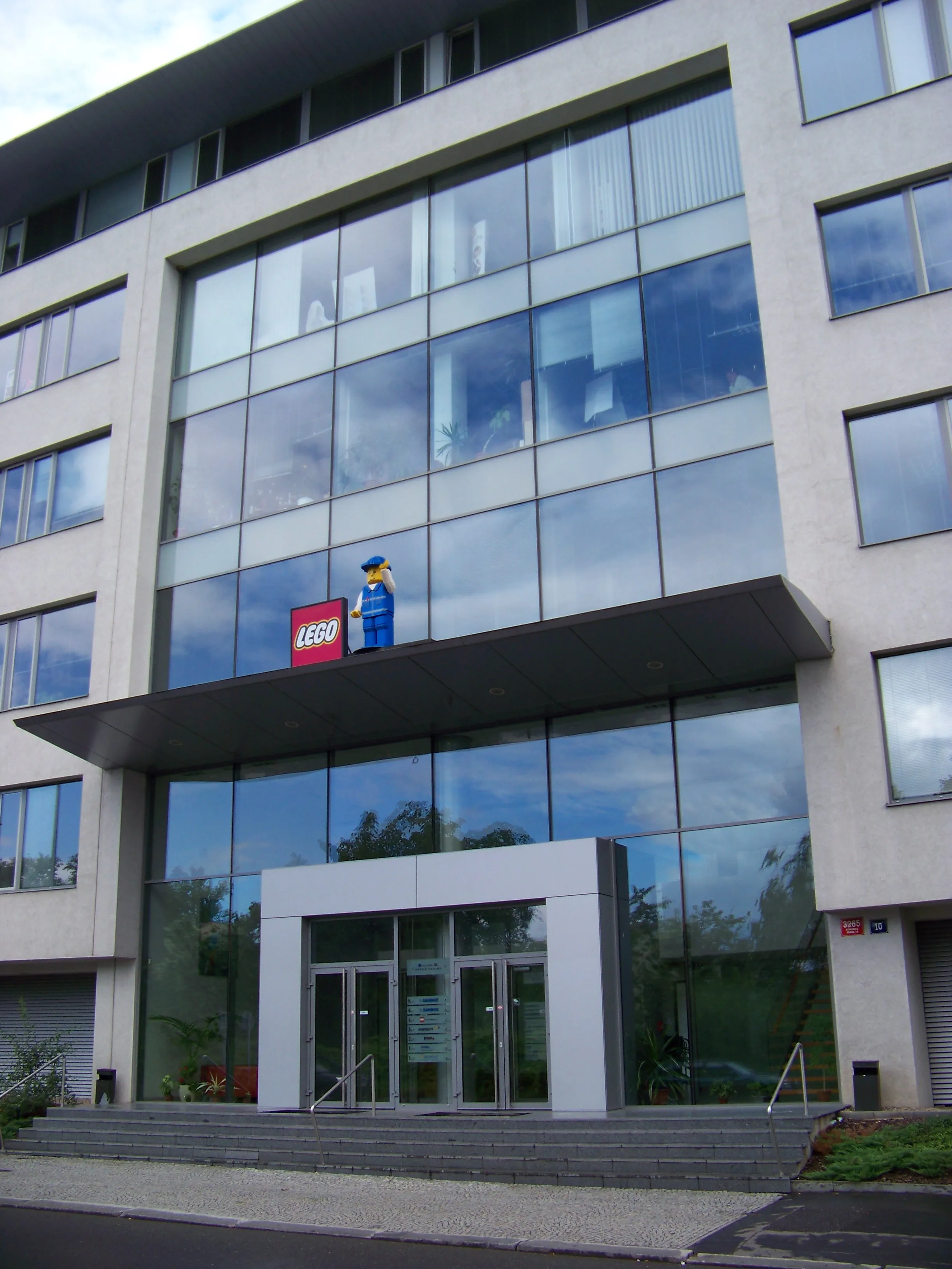 Modern gebouw met glazen gevel en LEGO-logo en minifiguur boven de ingang