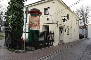 Un edificio de color claro con un letrero de buzón rojo y verde que dice 'Karikaturmuseum' y un emblema de pájaro negro sobre la entrada.