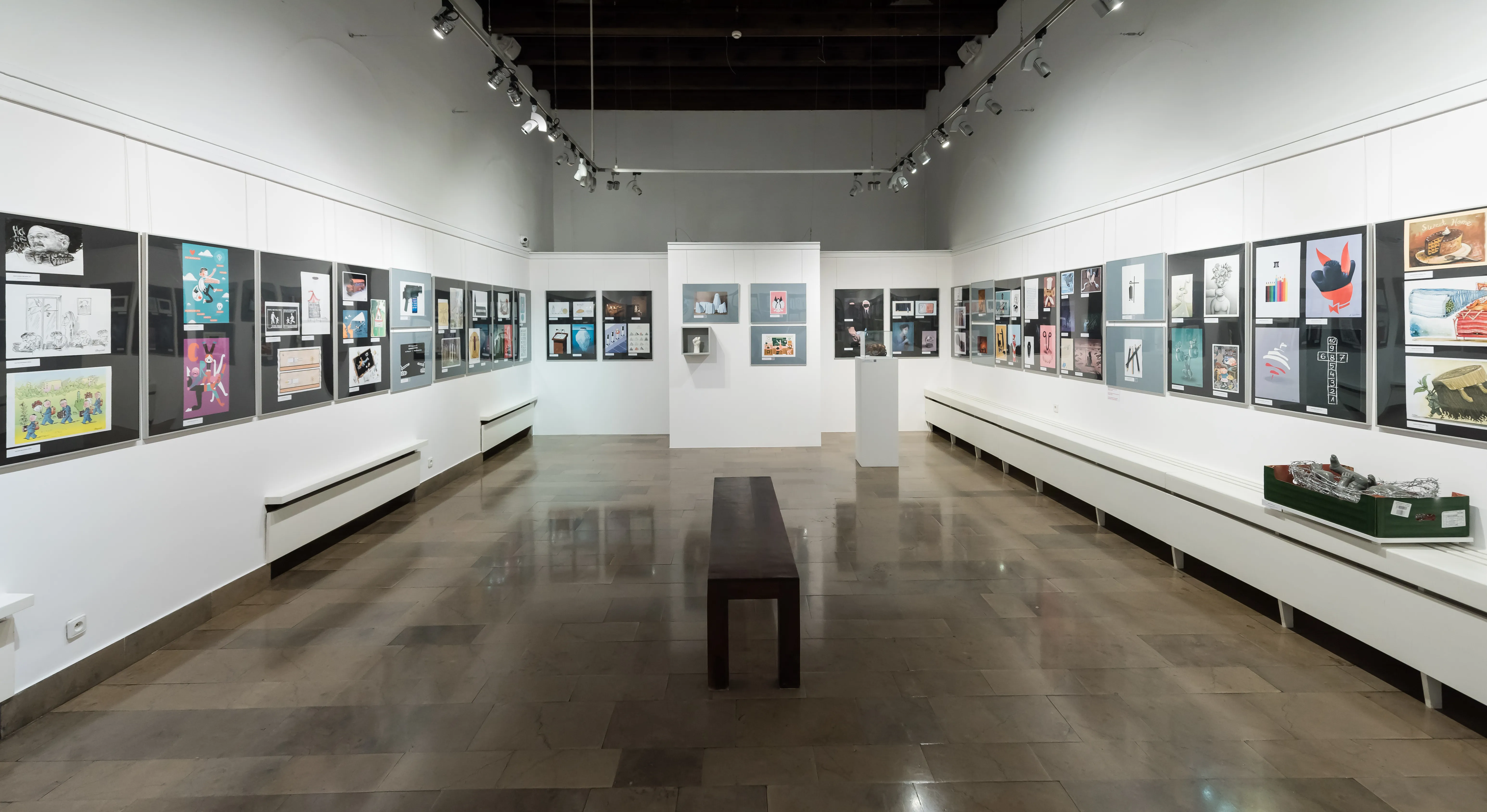 Larga galería con paredes blancas que exhiben obras de arte enmarcadas y un banco central