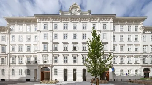 Edificio neoclásico blanco con ventanas simétricas y una torre de reloj central, con un árbol delante.