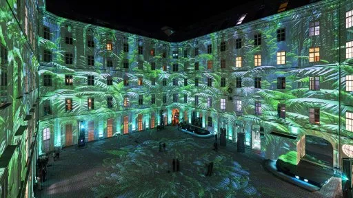 Un patio con muros de edificios históricos cubiertos de proyecciones verdes de patrones de hojas por la noche