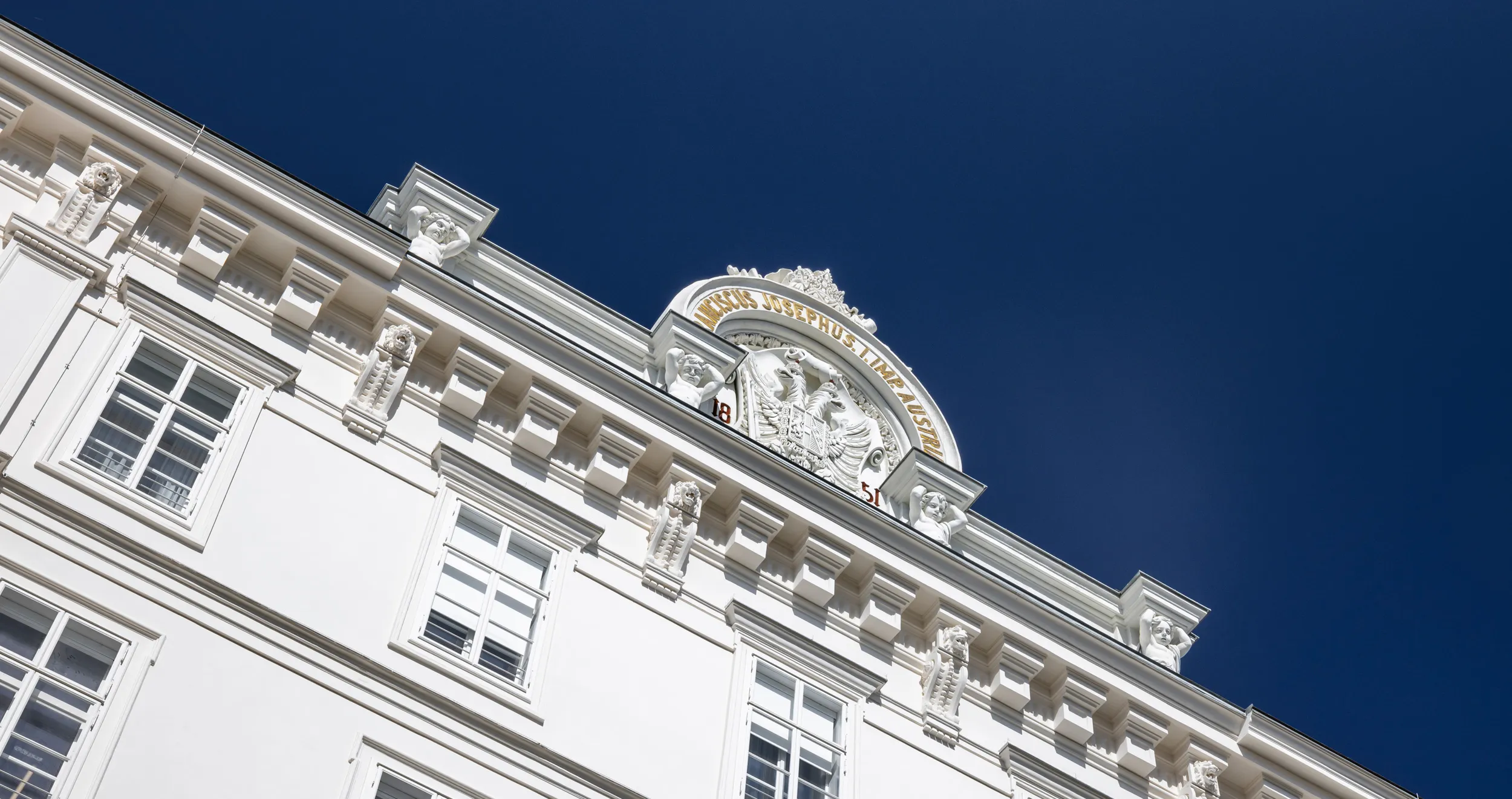 Fachada de edificio blanco y ornamentado con detalles arquitectónicos clásicos bajo un cielo azul