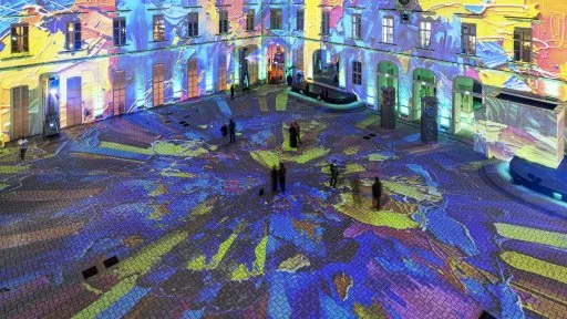 Proyecciones de luz colorida en un patio y fachada de edificio por la noche