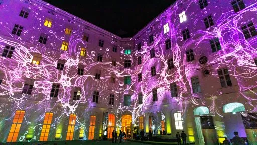 Exterior de un edificio grande por la noche con proyecciones de luz morada y naranja en las paredes y ventanas