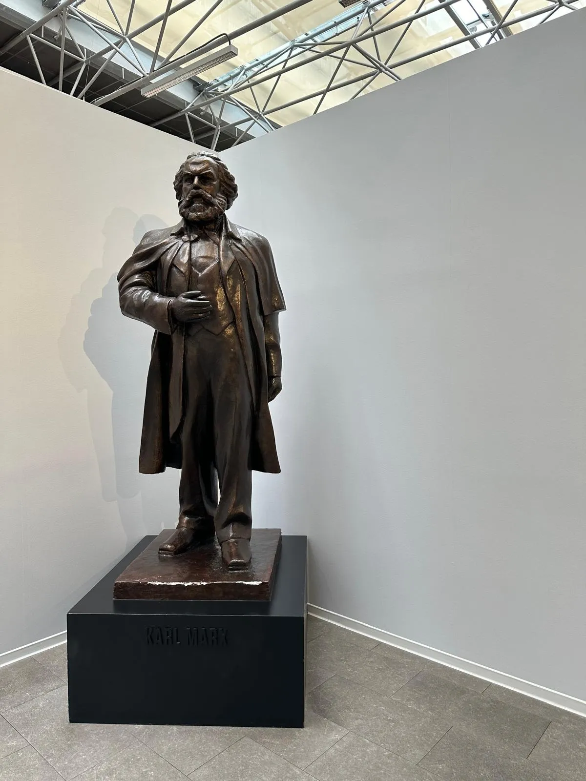 Estatua de bronce de Karl Marx sobre un pedestal negro en una galería de museo