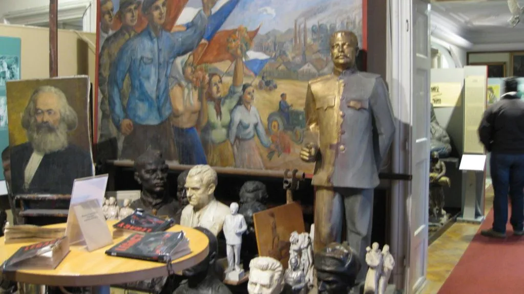 Interior de un museo con un gran mural, una estatua y varios bustos en exhibición.