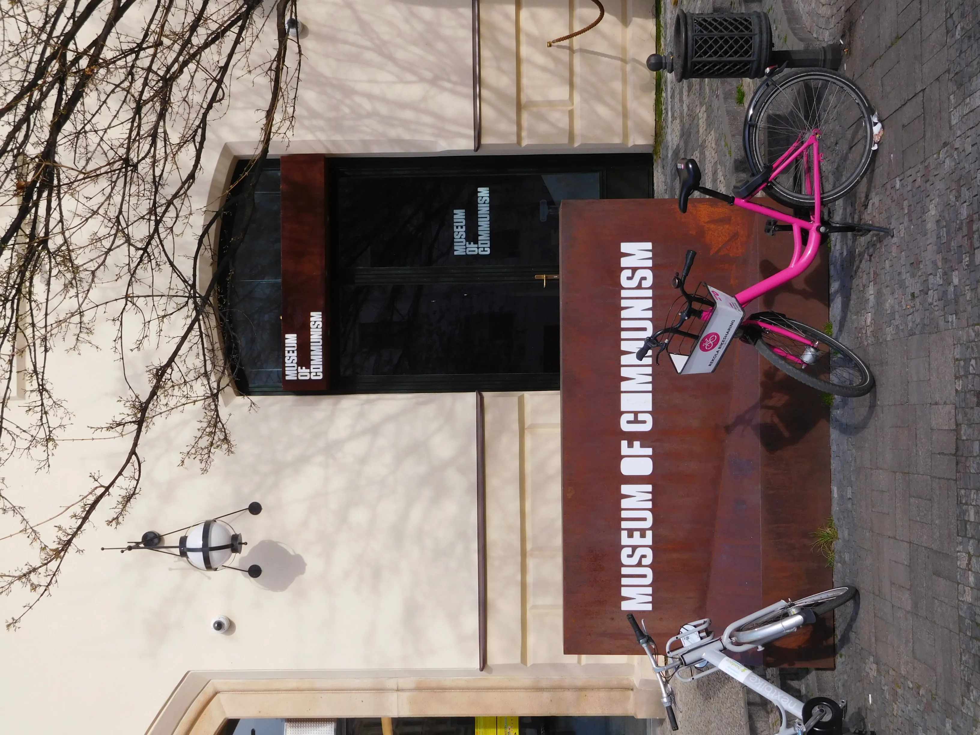 La entrada del Museo del Comunismo con un letrero y una bicicleta rosa aparcada afuera