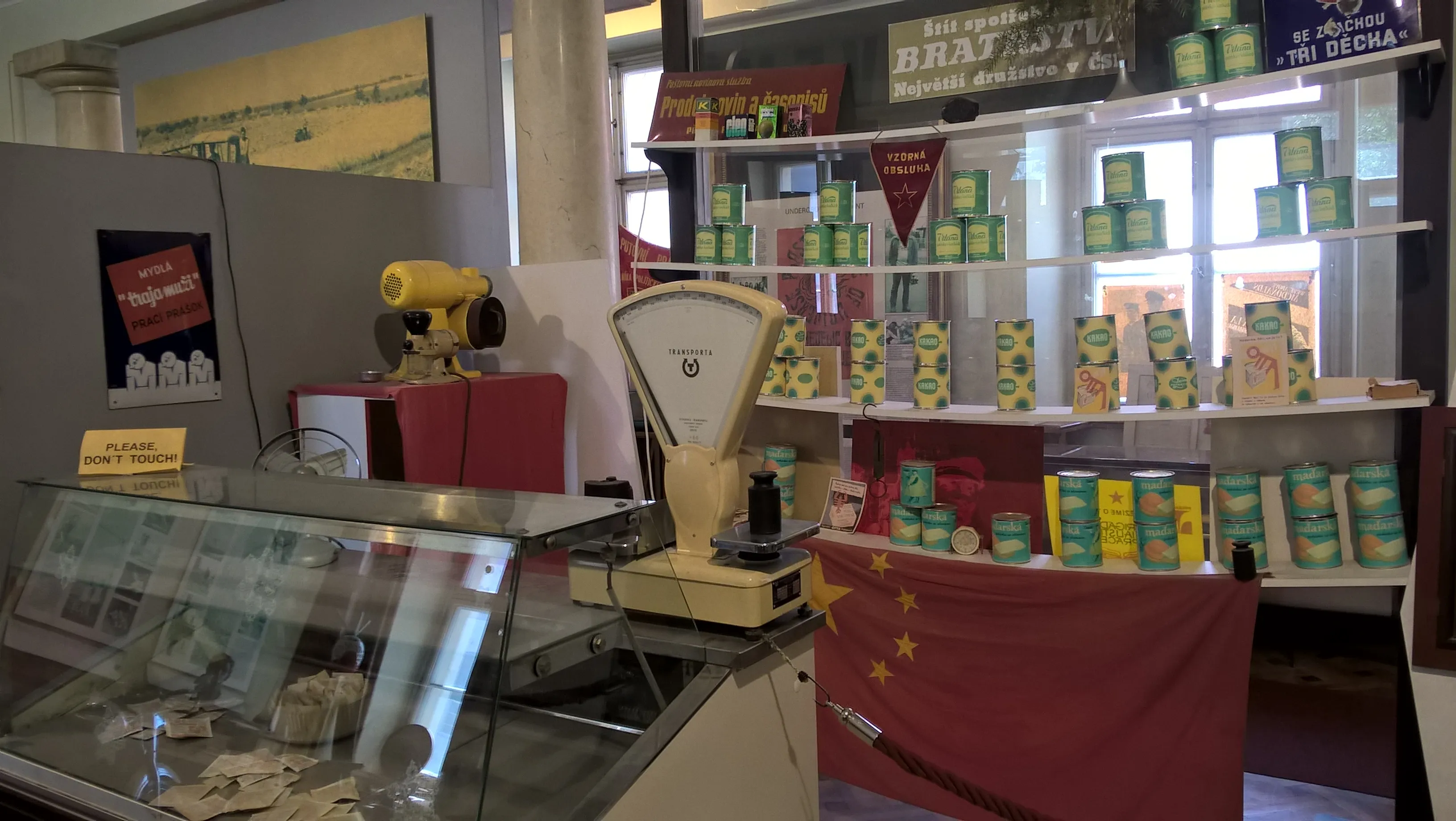 Tienda recreada de la era comunista con estantes de productos, una báscula y una bandera china