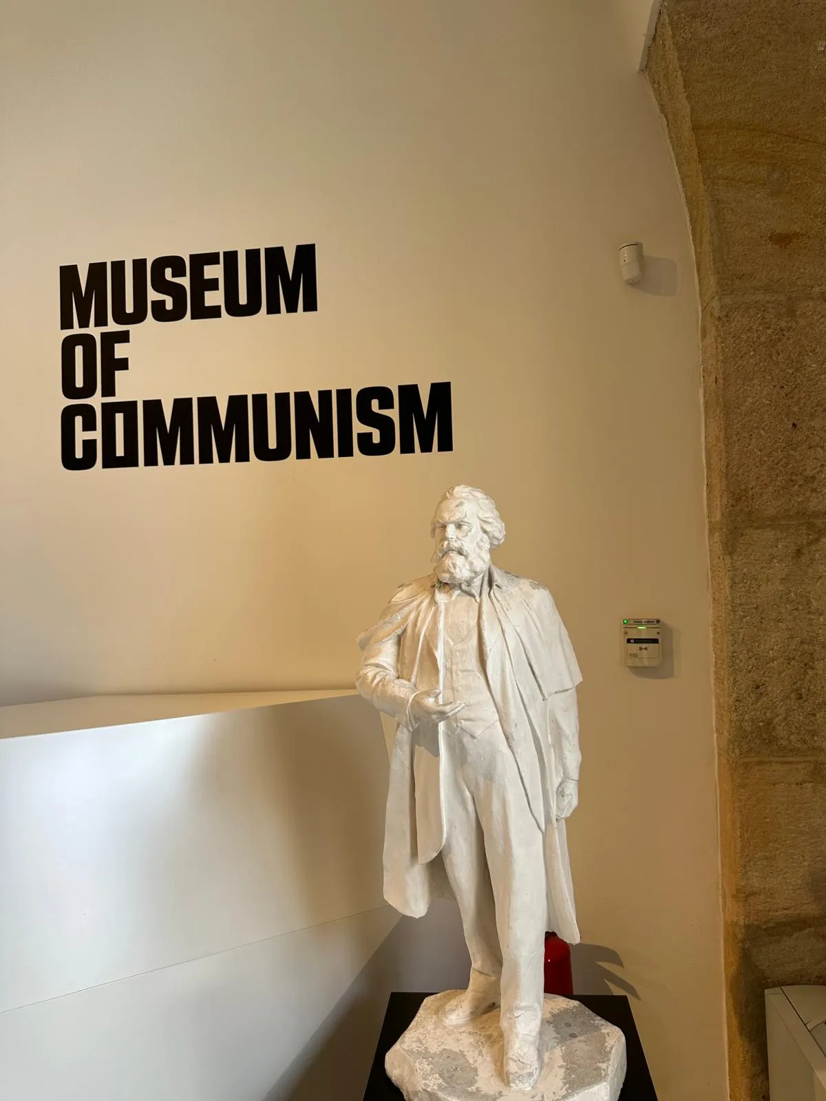 Una estatua blanca de Karl Marx se encuentra frente a una pared con las palabras 'MUSEUM OF COMMUNISM' en letras negras en negrita.