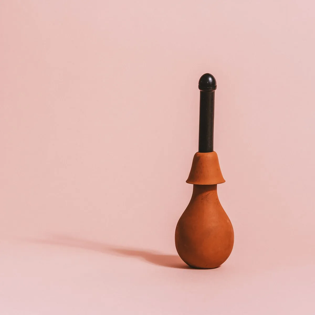 Un dispositivo de cerámica marrón con un asa negra sobre un fondo rosa