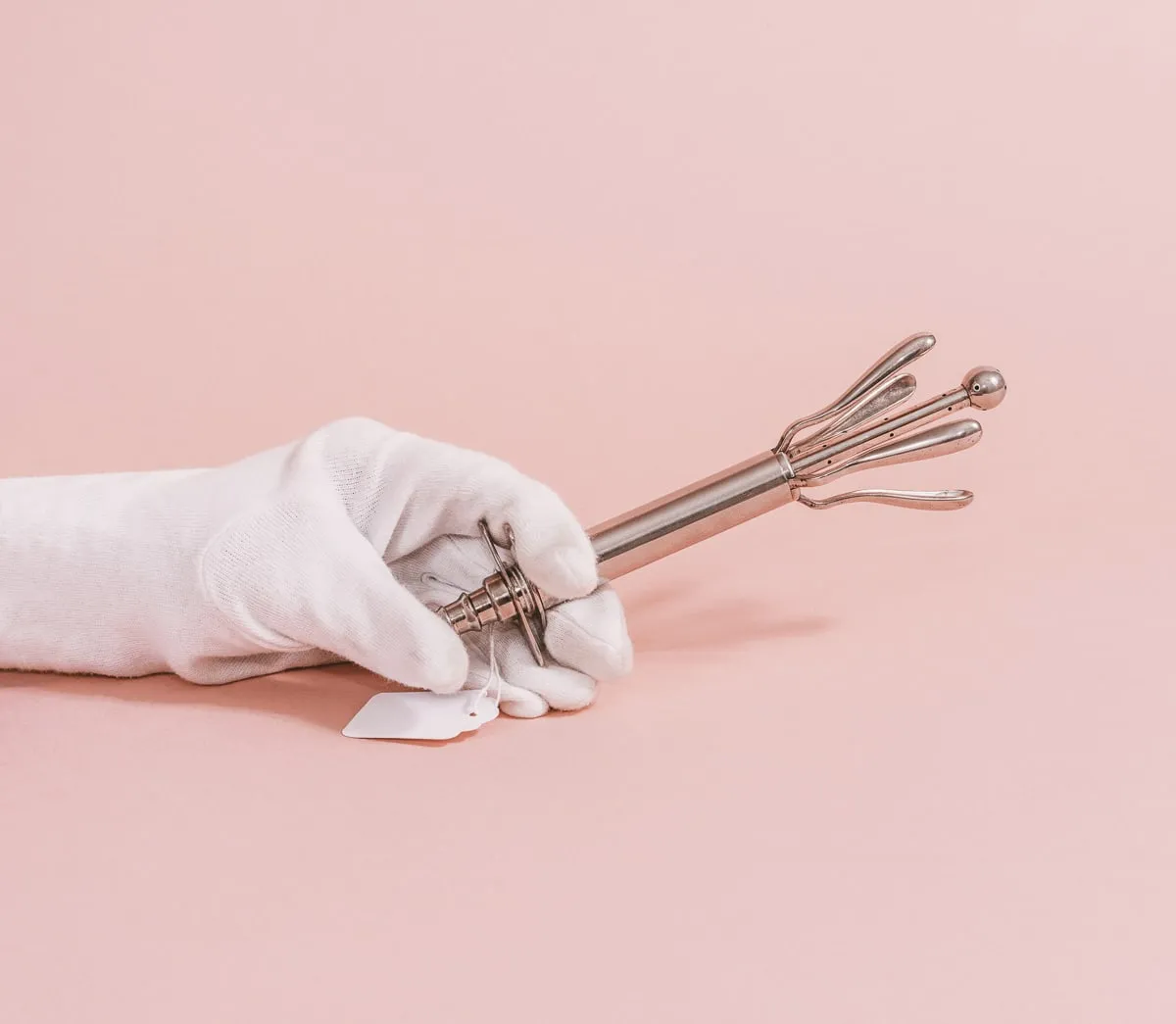 mano enguantada en blanco sosteniendo un instrumento médico metálico con múltiples puntas y una punta esférica