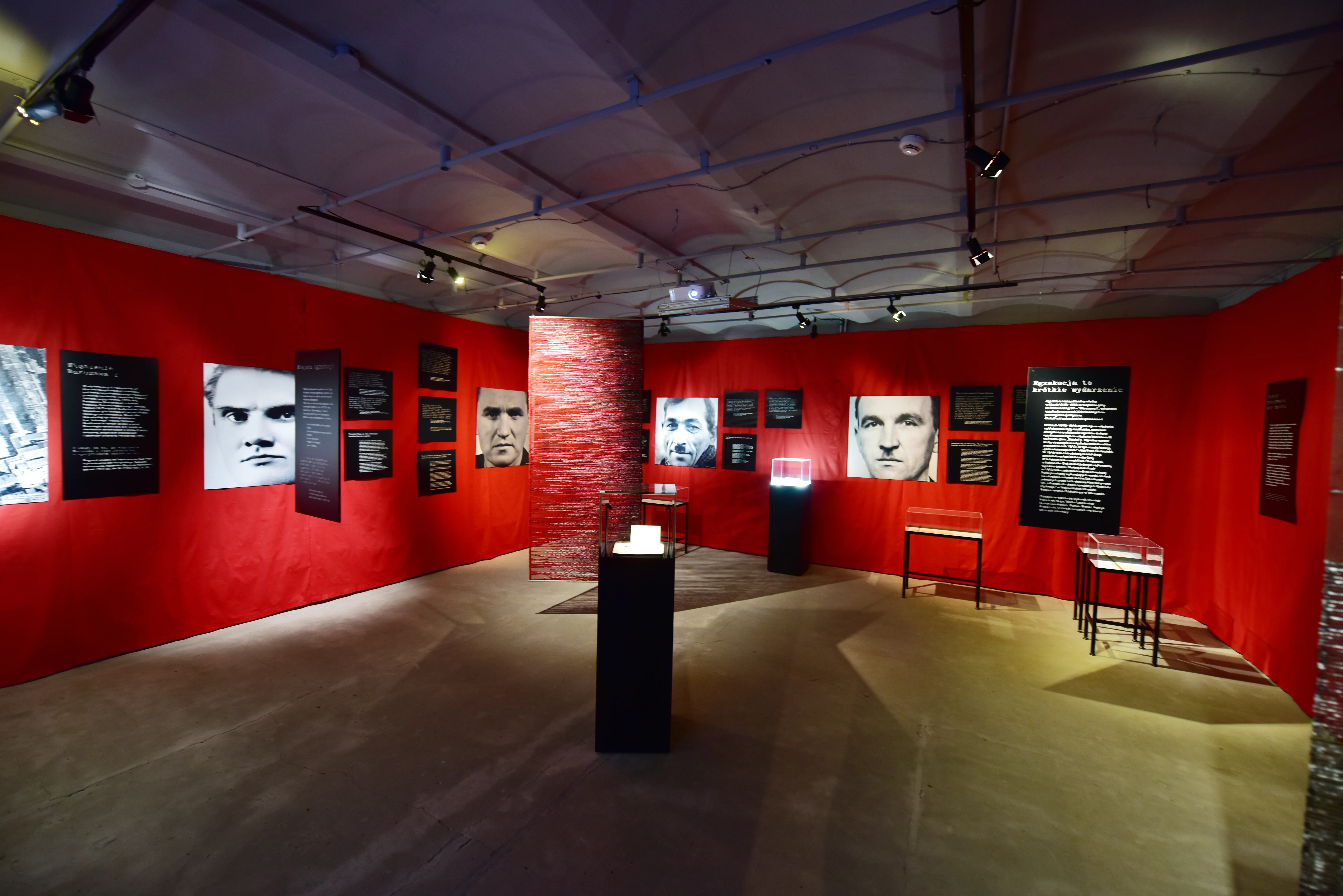 Interieur van een museumgalerij met rode muren, ingelijste portretten en vitrines