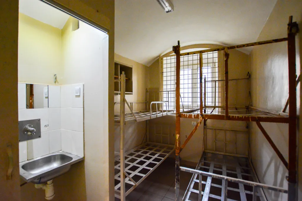 cel de prisión con literas de metal, ventana con rejas y lavabo
