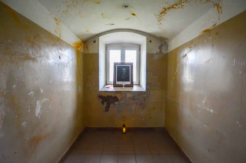 cel de prisión con paredes amarillentas desconchadas, una ventana arqueada y un retrato enmarcado en el alféizar