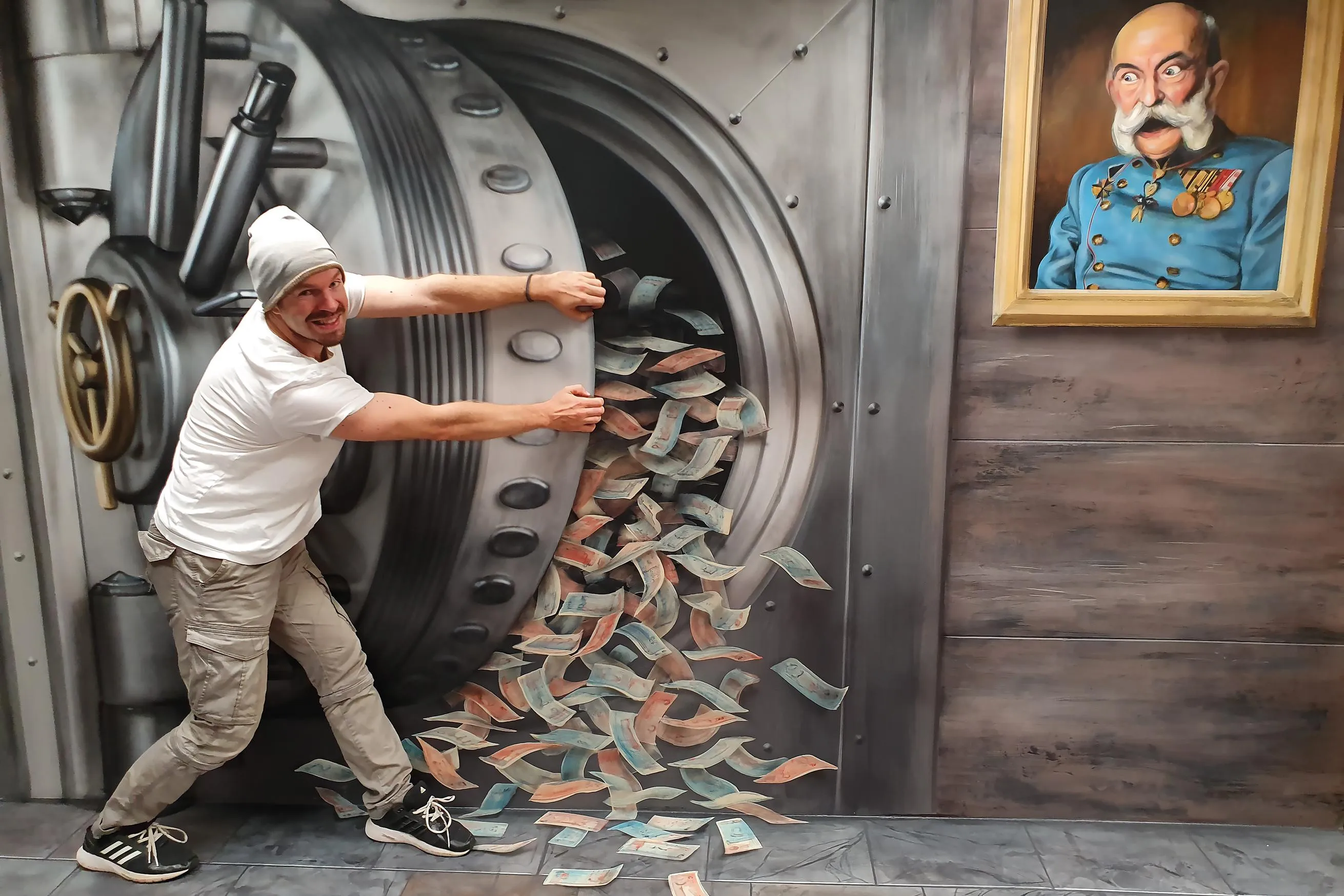 A man in a white t-shirt and beanie pushing a large bank vault door, with a 3D illusion of money falling out, next to a framed portrait of a man in a military uniform.