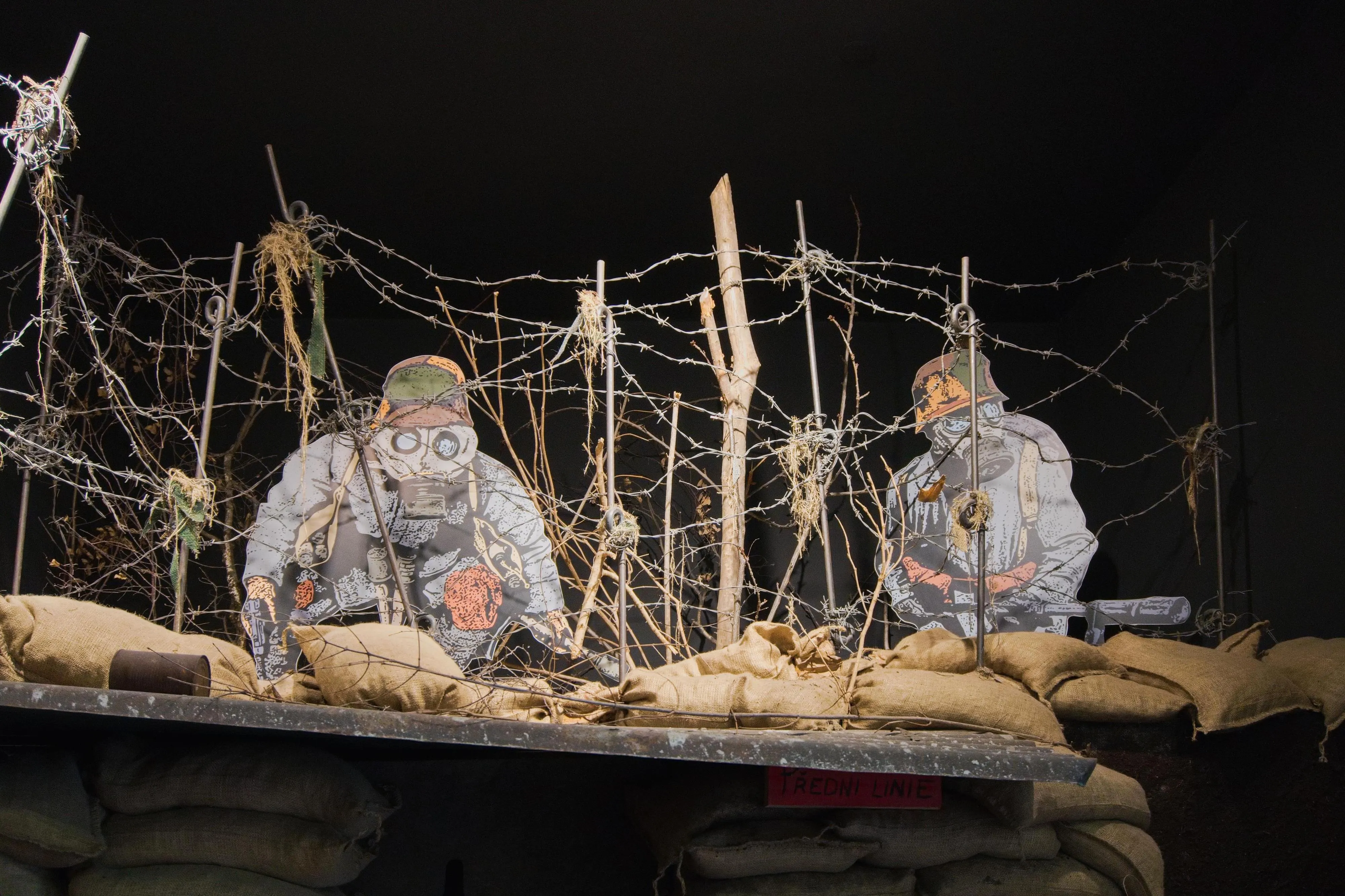 Two soldiers in gas masks behind barbed wire and sandbags