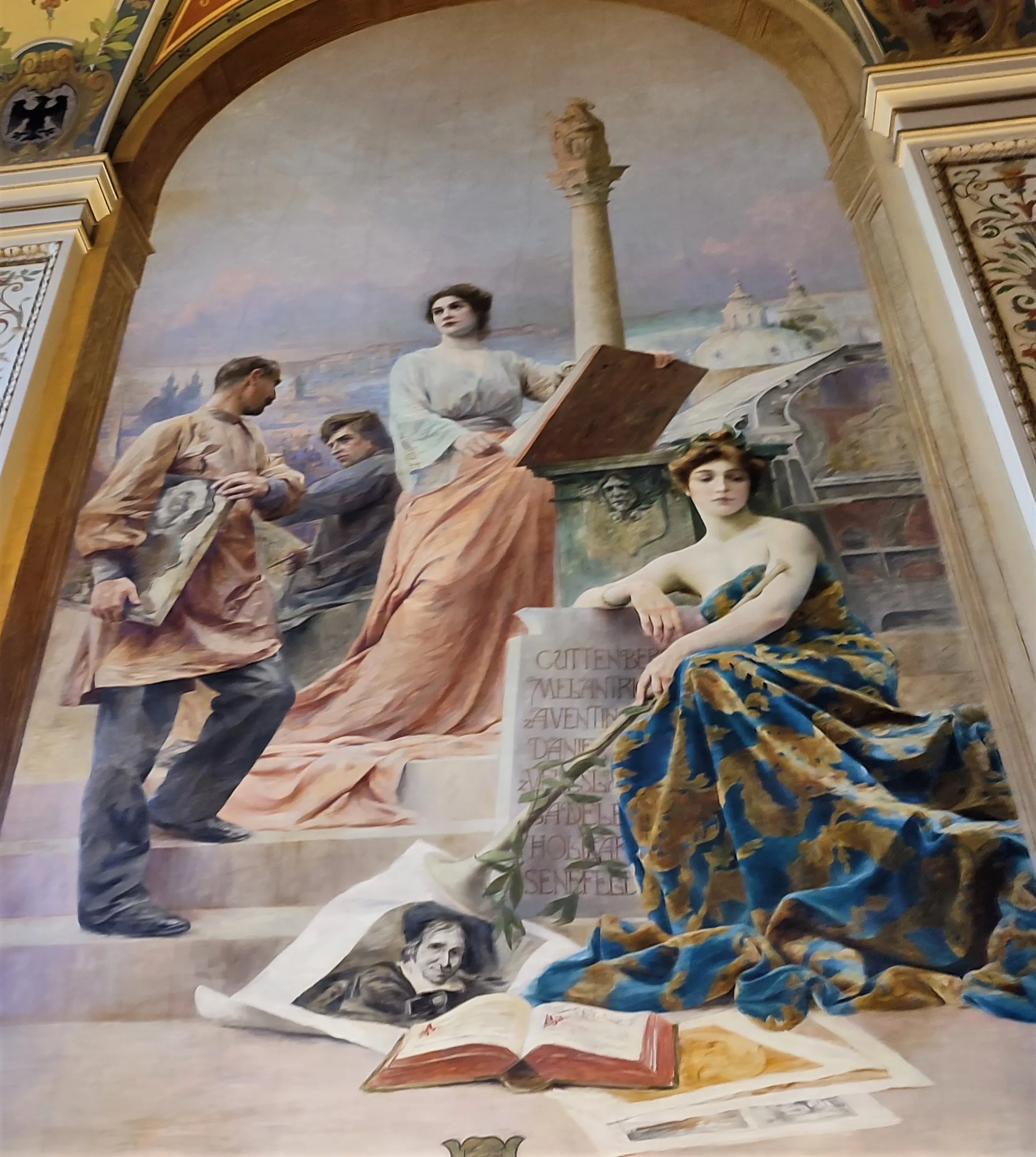 A large mural inside a museum featuring a woman in a blue and gold gown seated on steps, a central female figure holding a book, and other historical figures in a classical setting.