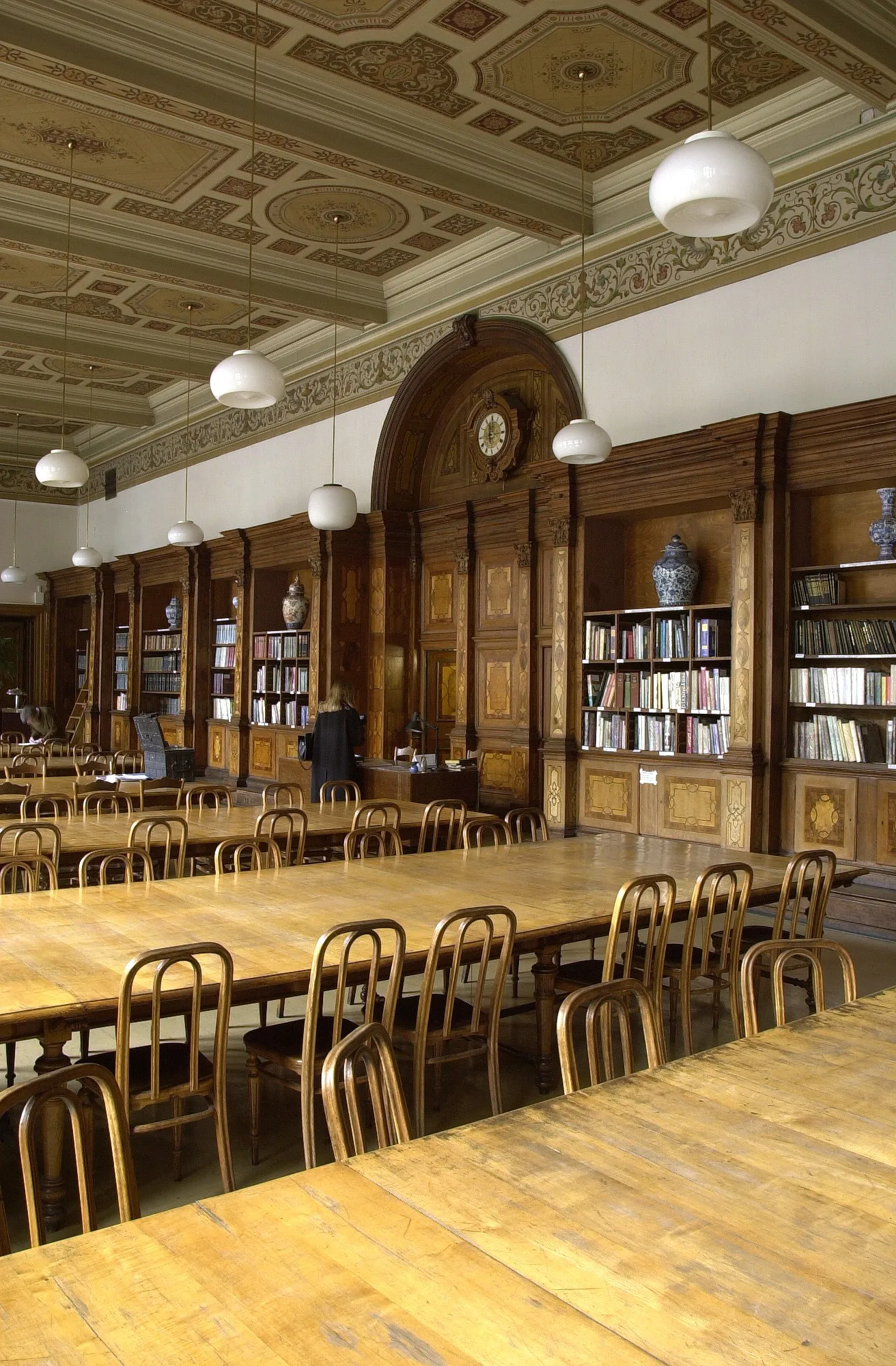 Wnętrze wspaniałej czytelni z drewnianymi stołami, krzesłami i regałami pod ozdobnym sufitem