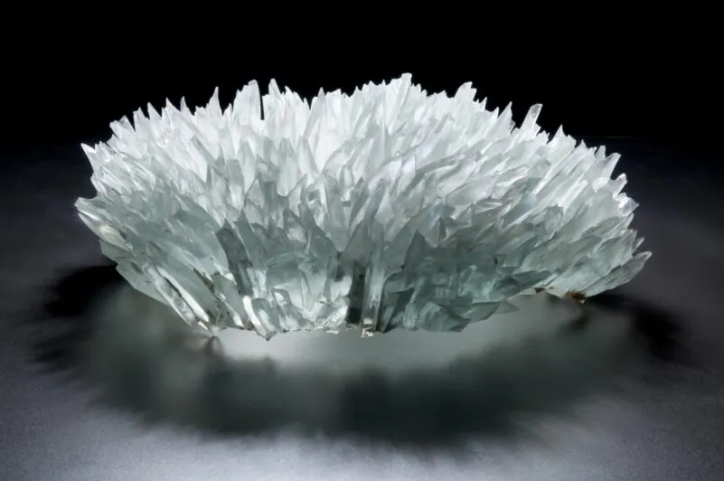 A white and translucent glass sculpture with spiky, crystalline formations on a dark surface