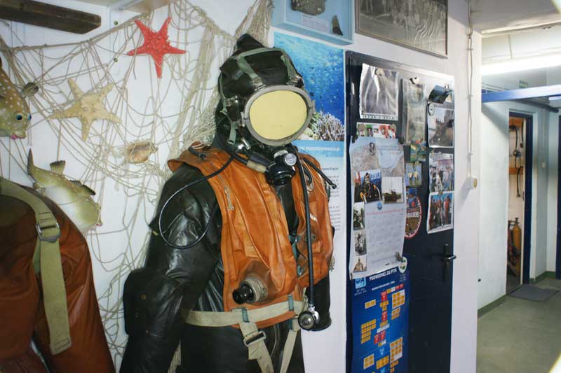 vintage diving suit with helmet and orange vest on display in a museum, surrounded by starfish and fishing net decorations
