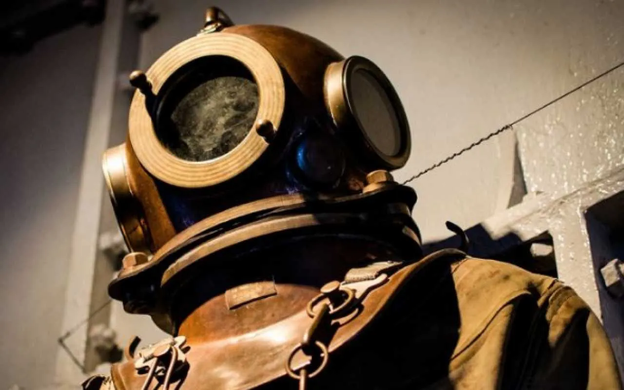 Zbliżenie zabytkowego hełmu nurkowego z mosiężnymi elementami i dużym szklanym wizjerem
