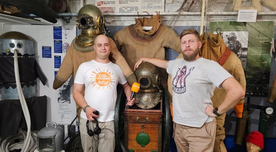 Two men standing in a museum exhibit with vintage diving helmets and suits