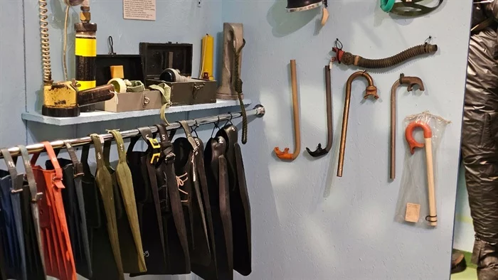 Diving equipment including suits, helmets, and tools displayed on a wall at the Museum of Diving