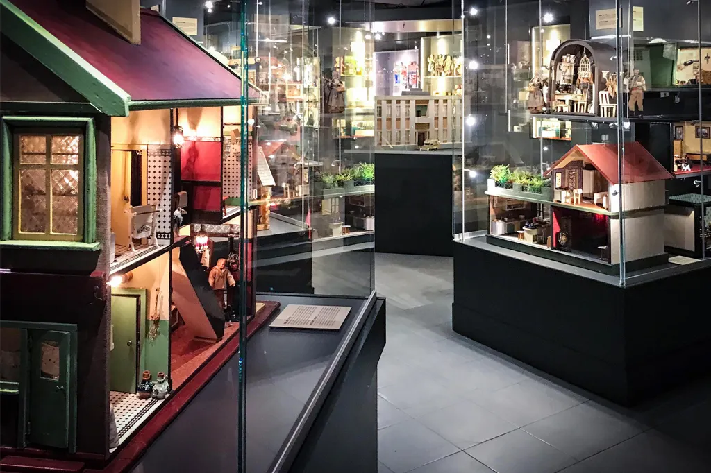 Glass display cases containing miniature dollhouses and toy interiors in a museum gallery