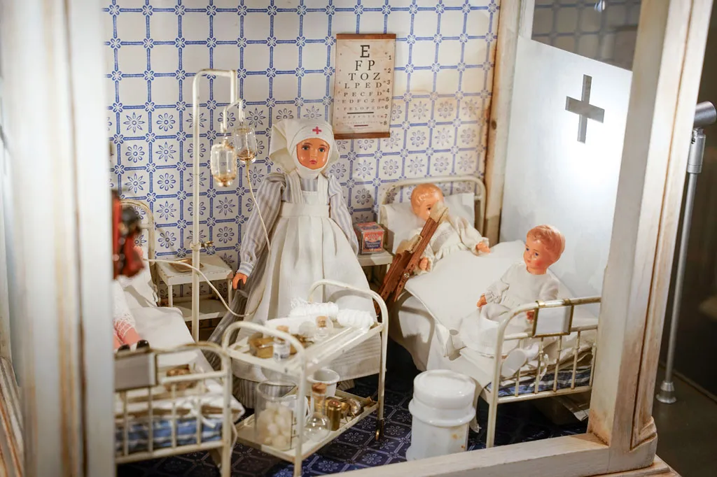 Miniature hospital ward with dolls in beds, medical equipment, and patterned tiles