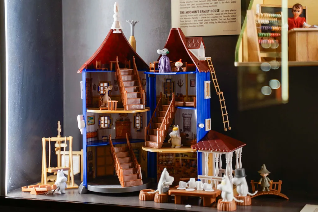 A multi-level miniature dollhouse with detailed interiors, stairs, and small figurines on display
