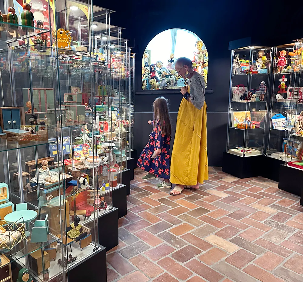 Two children looking at glass display cases filled with toys and dollhouses in a museum gallery