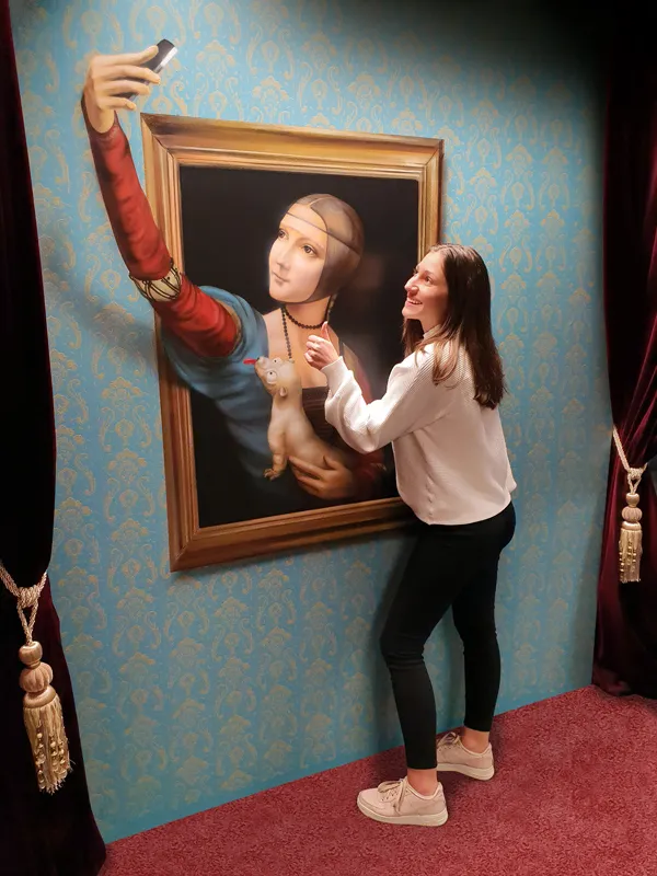 Kobieta robiąca sobie selfie z obrazem iluzji 3D przedstawiającym kobietę w czerwonym rękawie wyciągającą rękę z kadru